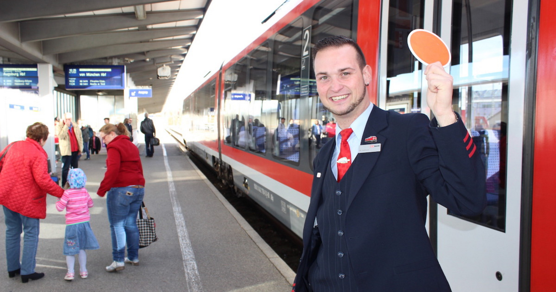 Ein Zugbegleiter steht vor einem Zug und lächelt.