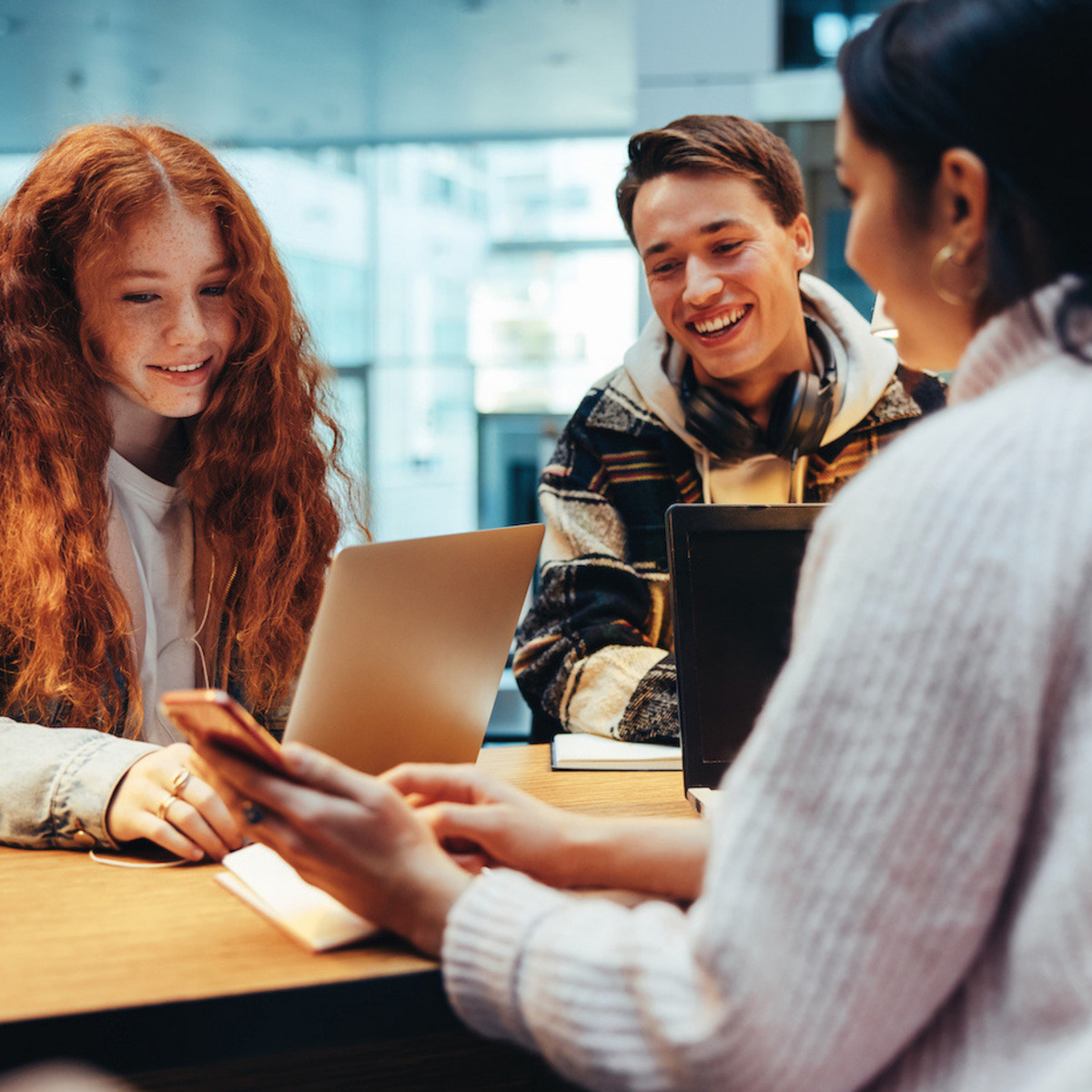 Drei Schüler:innen sitzen an einem Tisch und schauen sich etwas auf dem Handy an.