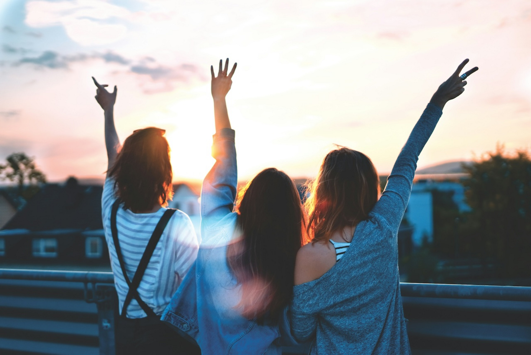 Drei Frauen strecken die Arme in den Sonnenuntergang
