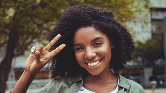 Eine Frau lächelt und macht mit ihrer Hand das Friedenszeichen.