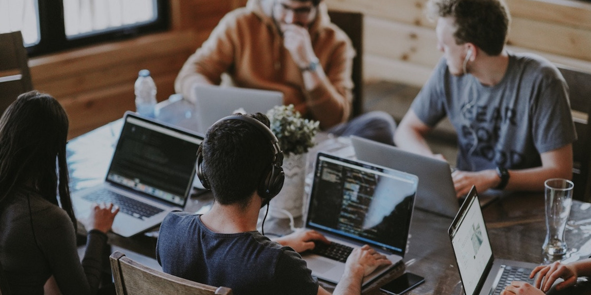 Vier Menschen sitzen mit Laptops an einem Tisch.