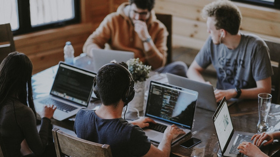 Vier Menschen sitzen mit Laptops an einem Tisch.