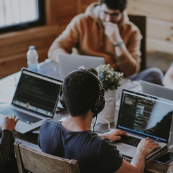 Vier Menschen sitzen mit Laptops an einem Tisch.