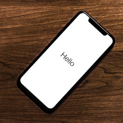 Ein Smartphone mit dem Text "Hello" auf dem Schirm liegt auf einem Holztisch.