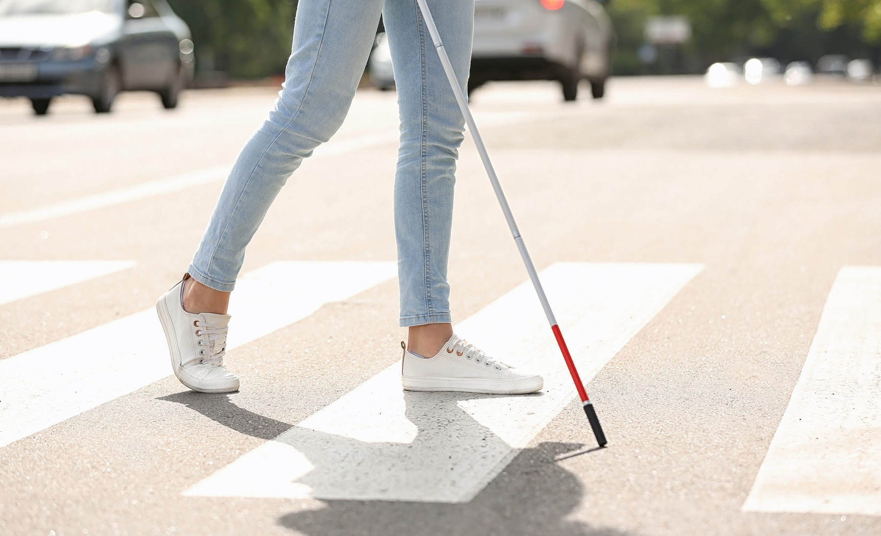 Eine blinde Frau überquert mithilfe eines Langstocks einen Zebrastreifen.