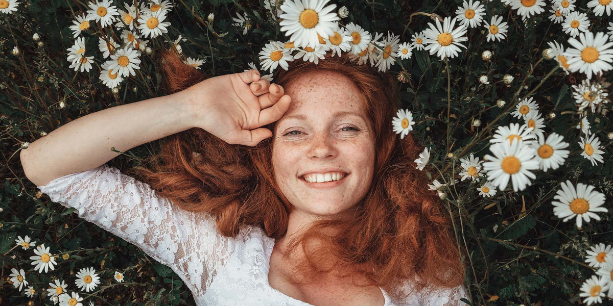 Eine junge, glückliche Frau liegt auf einer Wiese mit vielzähligen Kamillenblüten