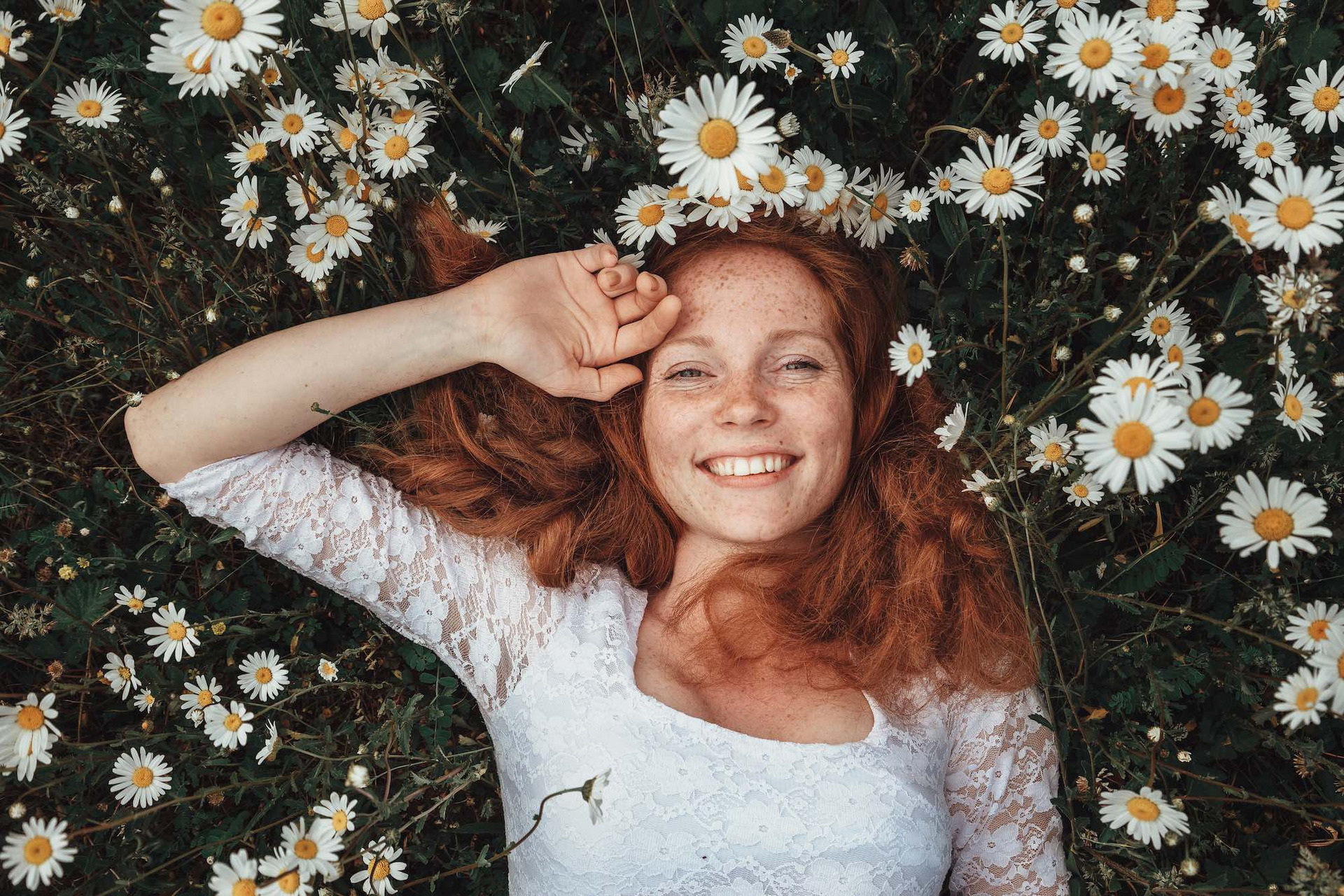 Eine junge, glückliche Frau liegt auf einer Wiese mit vielzähligen Kamillenblüten