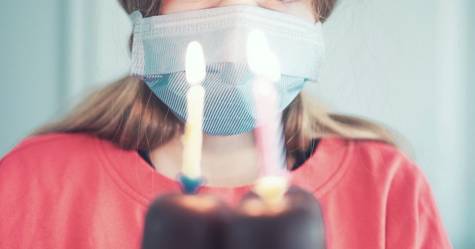 Eine Person mit Maske steht vor einer Torte mit drei Geburtstagskerzen.