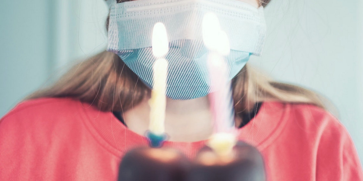 Eine Person mit Maske steht vor einer Torte mit drei Geburtstagskerzen.