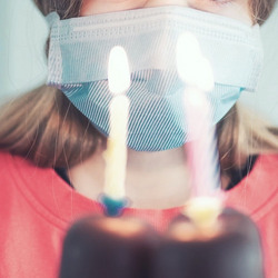 Eine Person mit Maske steht vor einer Torte mit drei Geburtstagskerzen.