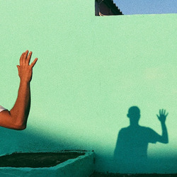 Der Schatten einer winkenden Person gegen eine grüne Wand