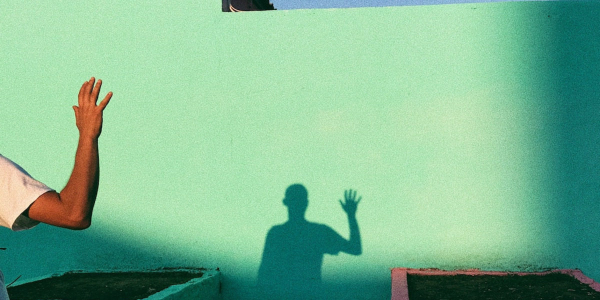 Der Schatten einer winkenden Person gegen eine grüne Wand