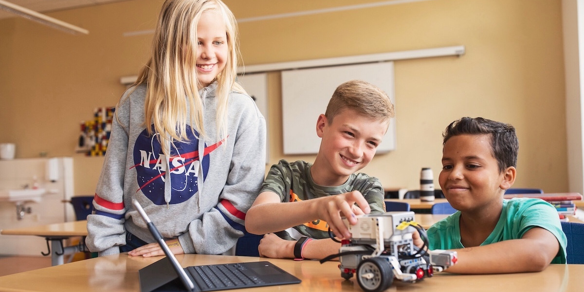 Drei Jugendlichen programmieren einen Roboter in einem Klassenzimmer.