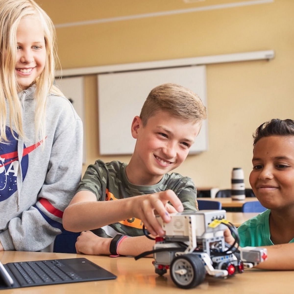 Drei Jugendlichen programmieren einen Roboter in einem Klassenzimmer.