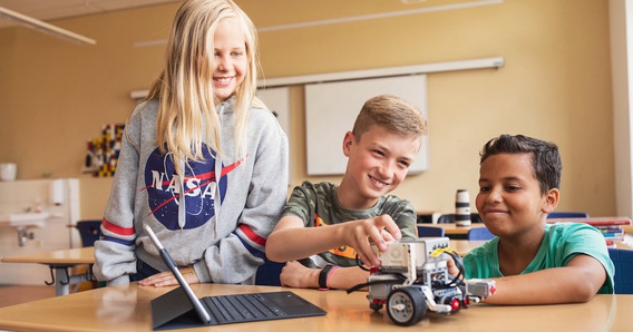 Drei Jugendlichen programmieren einen Roboter in einem Klassenzimmer.