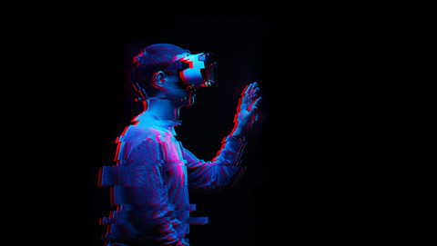 Eine Person trägt eine Virtual-Reality-Brille und greift mit der Hand in der Luft.