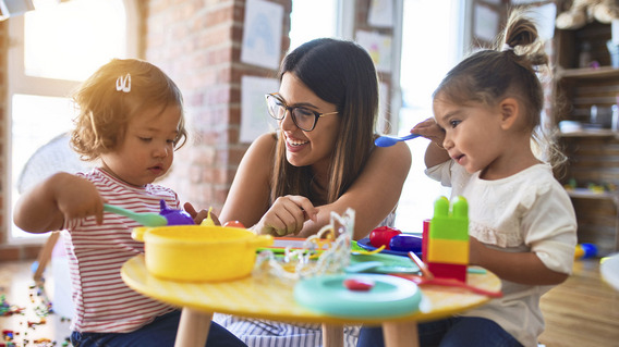 Eine junge Frau spielt lachend mit zwei Kindern in einer Kindertagesstätte