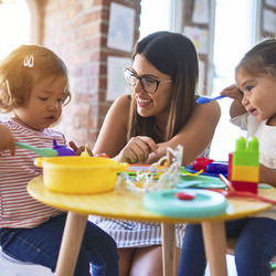 Eine junge Frau spielt lachend mit zwei Kindern in einer Kindertagesstätte