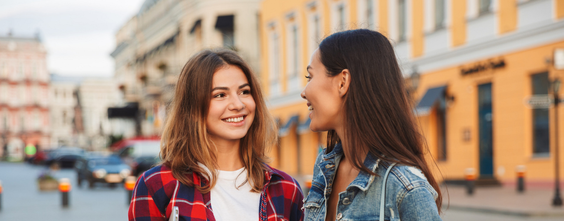 Zwei junge Frauen stehen auf einem Platz und lächeln sich an.