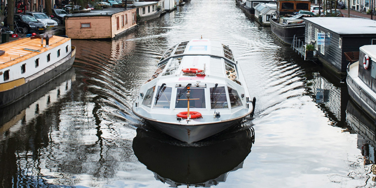 Ein Ausflugsboot fährt durch eine Gracht in Amsterdam
