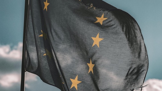 Die Flagge der Europäischen Union weht im Wind vor blauem Himmel. Der dunkelblaue Stoff mit den charakteristischen goldenen Sternen im Kreis ist in Bewegung und zeigt leichte Falten.