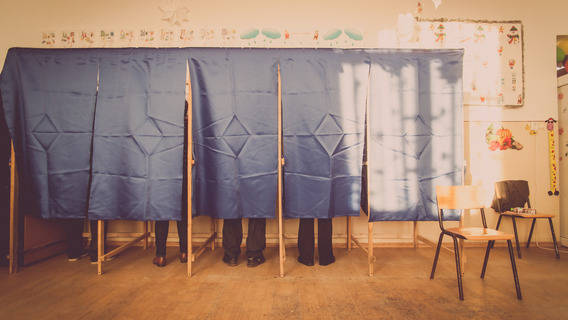 Menschen stehen hinter Vorhängen in Wahlkabinen