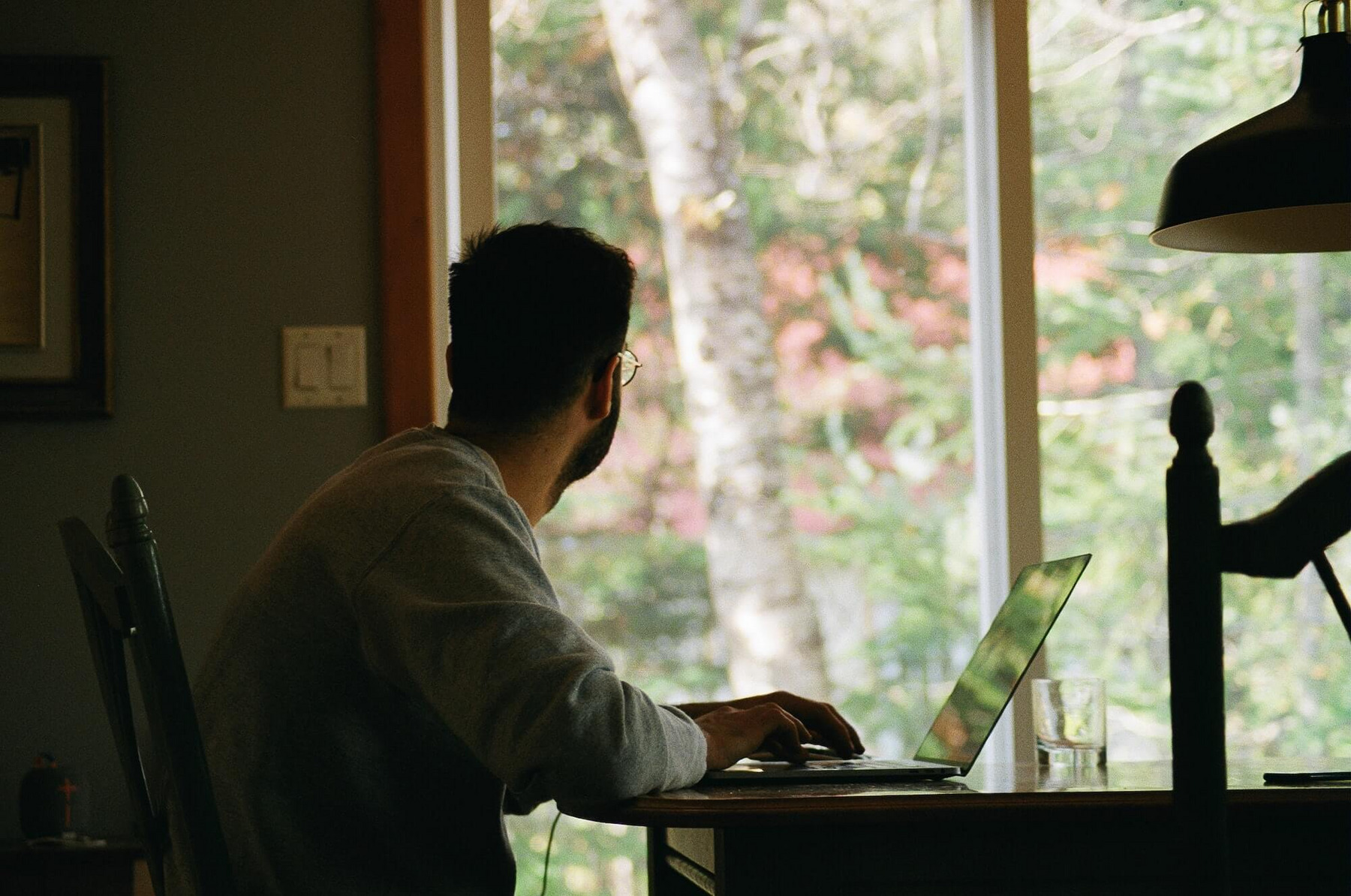Ein junger Mann sitzt in seiner Wohnung vor dem Laptop und schaut wehmütig aus dem Fenster