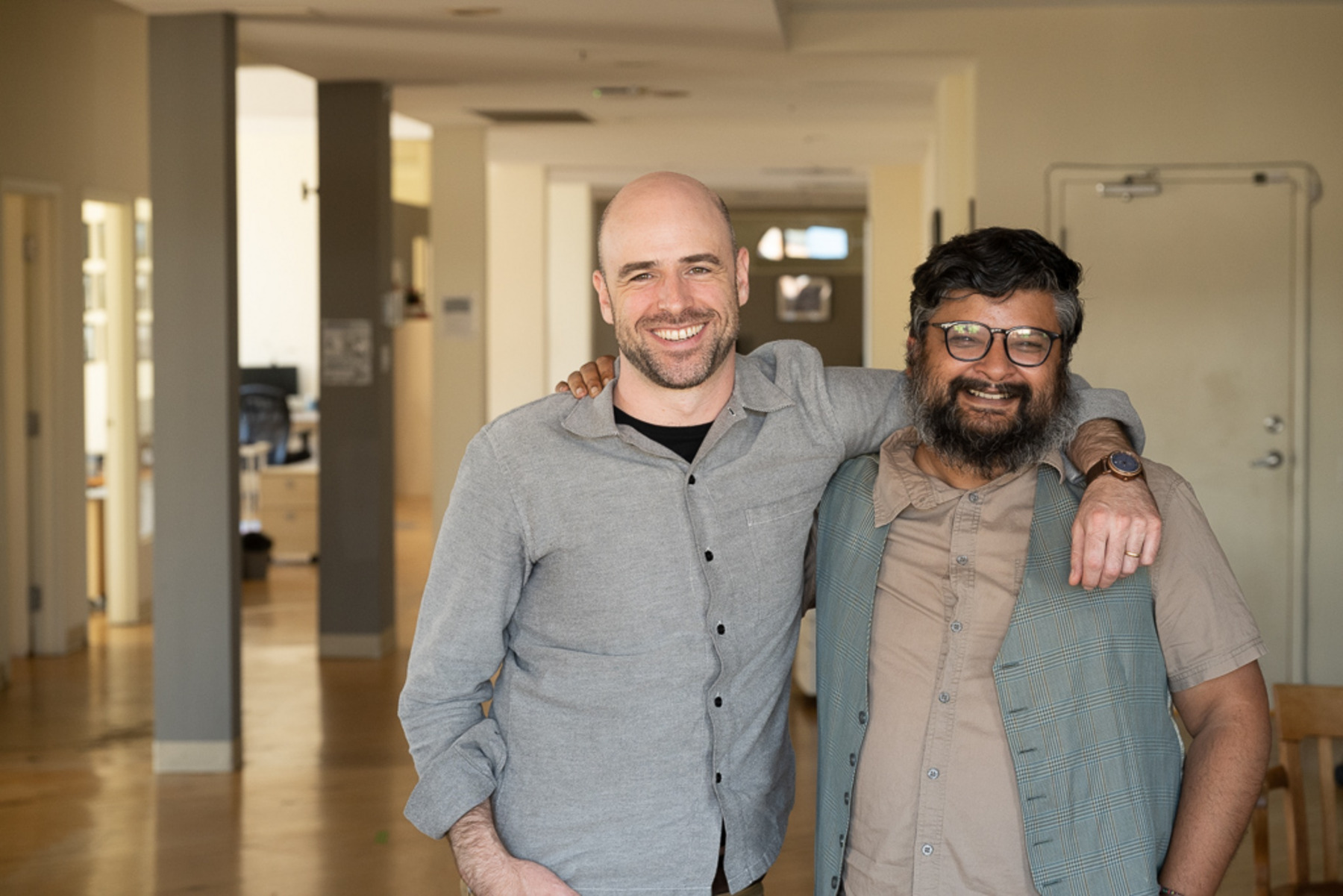 Daniel Bernhard, der CEO des Institute for Canadian Citizenship (ICC), und Tarun Tripathi, der Direktor der Canoo-App für kanadische Neubürger:innen, stehen zusammen vor der Kamera, lächeln und haben sich im Arm.