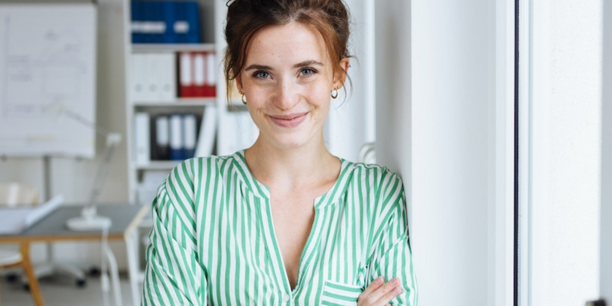 Eine junge Frau lehnt in einem Büro lächelnd an der Wand