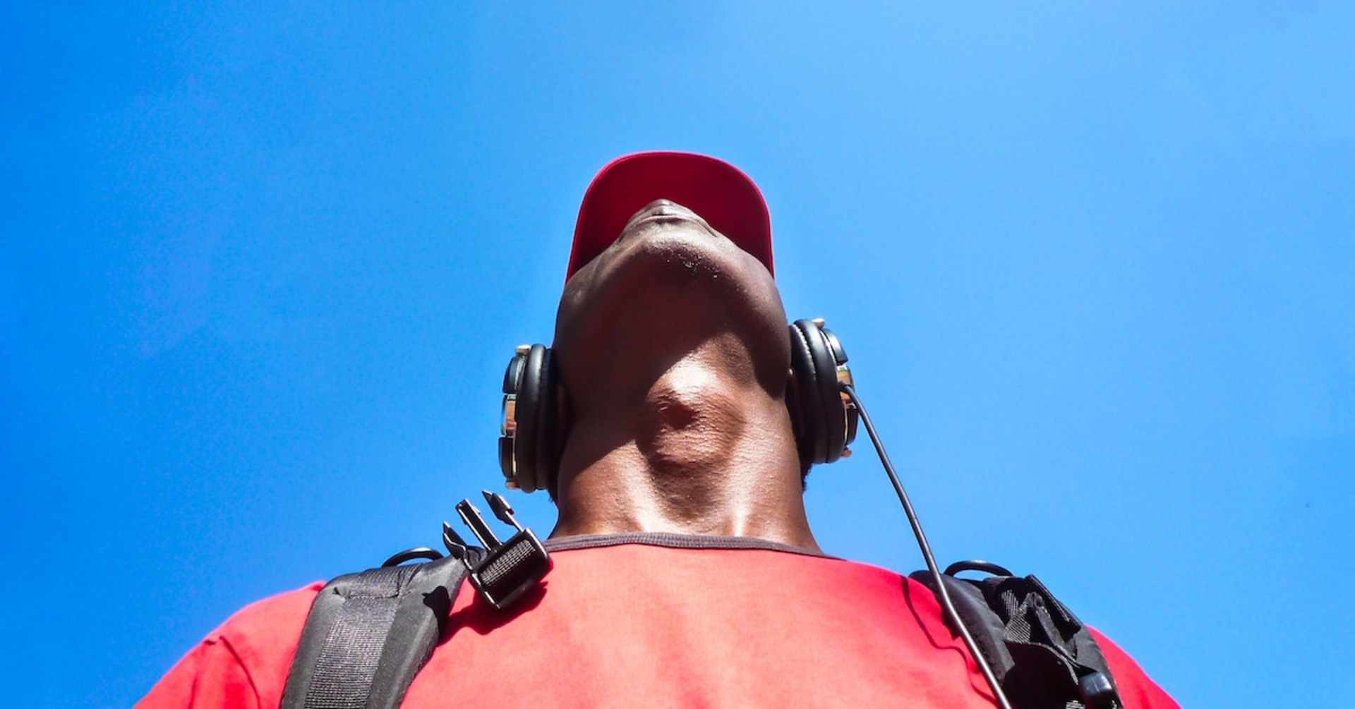 Eine Person mit Kopfhörern und einem roten T-Shirt schaut in den blauen Himmel.