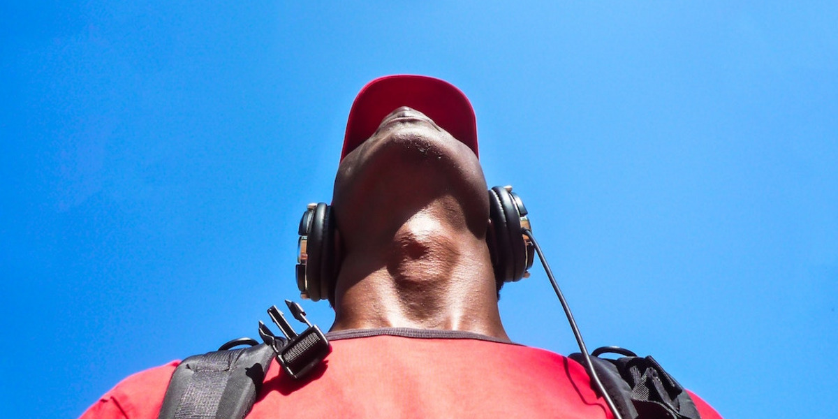 Eine Person mit Kopfhörern und einem roten T-Shirt schaut in den blauen Himmel.