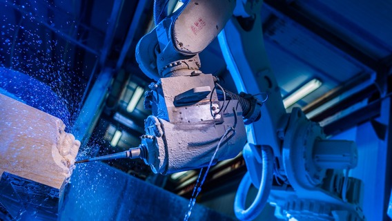 Ein Industrieroboter führt eine Bohrarbeit an einem Werkstück aus, aufgenommen in blauer Beleuchtung. Die Szene zeigt moderne Fertigungstechnologie in einem Steinmetzbetrieb.