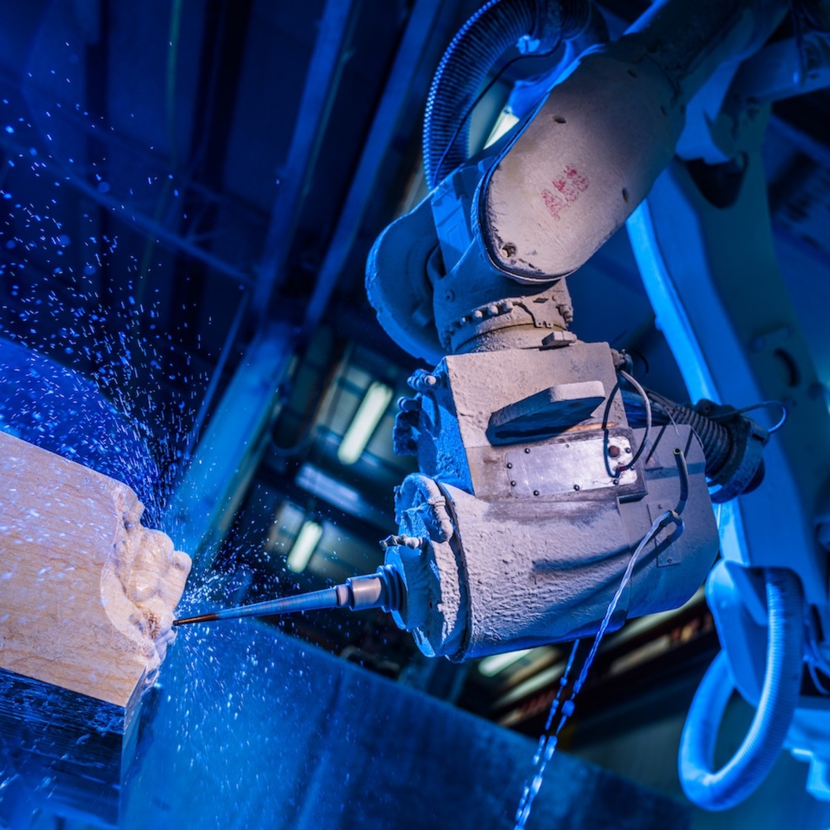 Ein Industrieroboter führt eine Bohrarbeit an einem Werkstück aus, aufgenommen in blauer Beleuchtung. Die Szene zeigt moderne Fertigungstechnologie in einem Steinmetzbetrieb.