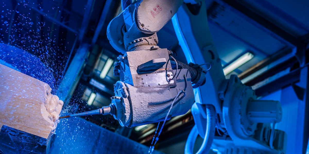 Ein Industrieroboter führt eine Bohrarbeit an einem Werkstück aus, aufgenommen in blauer Beleuchtung. Die Szene zeigt moderne Fertigungstechnologie in einem Steinmetzbetrieb.