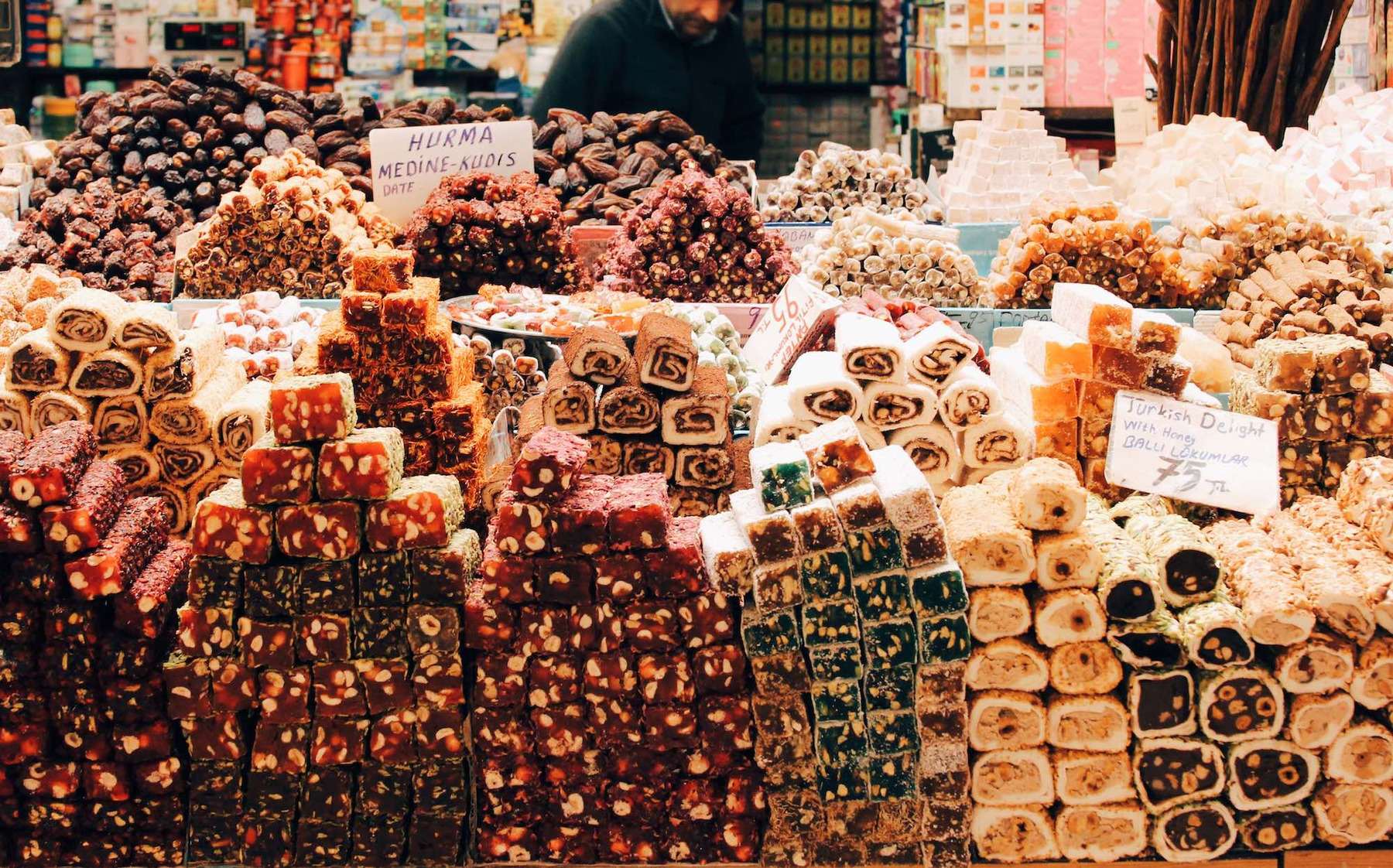 Eine große Auswahl an Süßigkeiten auf einem Markt in Istanbul: Ein Mann in schwarzer Jacke steht vor riesigen Mengen Gebäck und Süßigkeiten an seinem Marktstand.