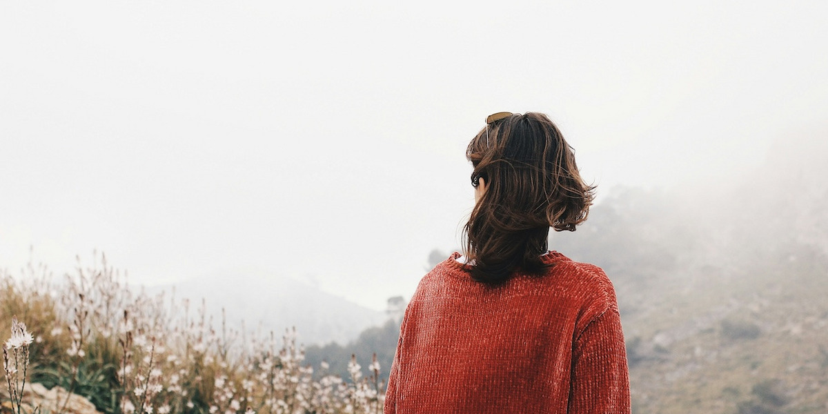Eine Frau blickt auf eine karge Berglandschaft im Nebel