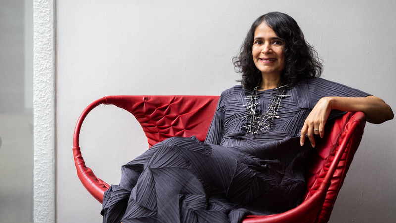 Malavika Jayaram sitzt in einem roten Sessel und lächelt