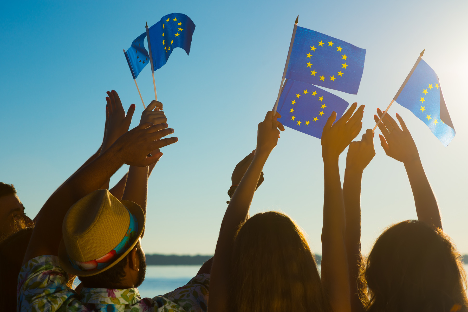shutterstock_334006058_Premier_ST-CC.jpg Junge Männer und Frauen halten Fähnchen mit der Flagge der Europäischen Union in die Luft.