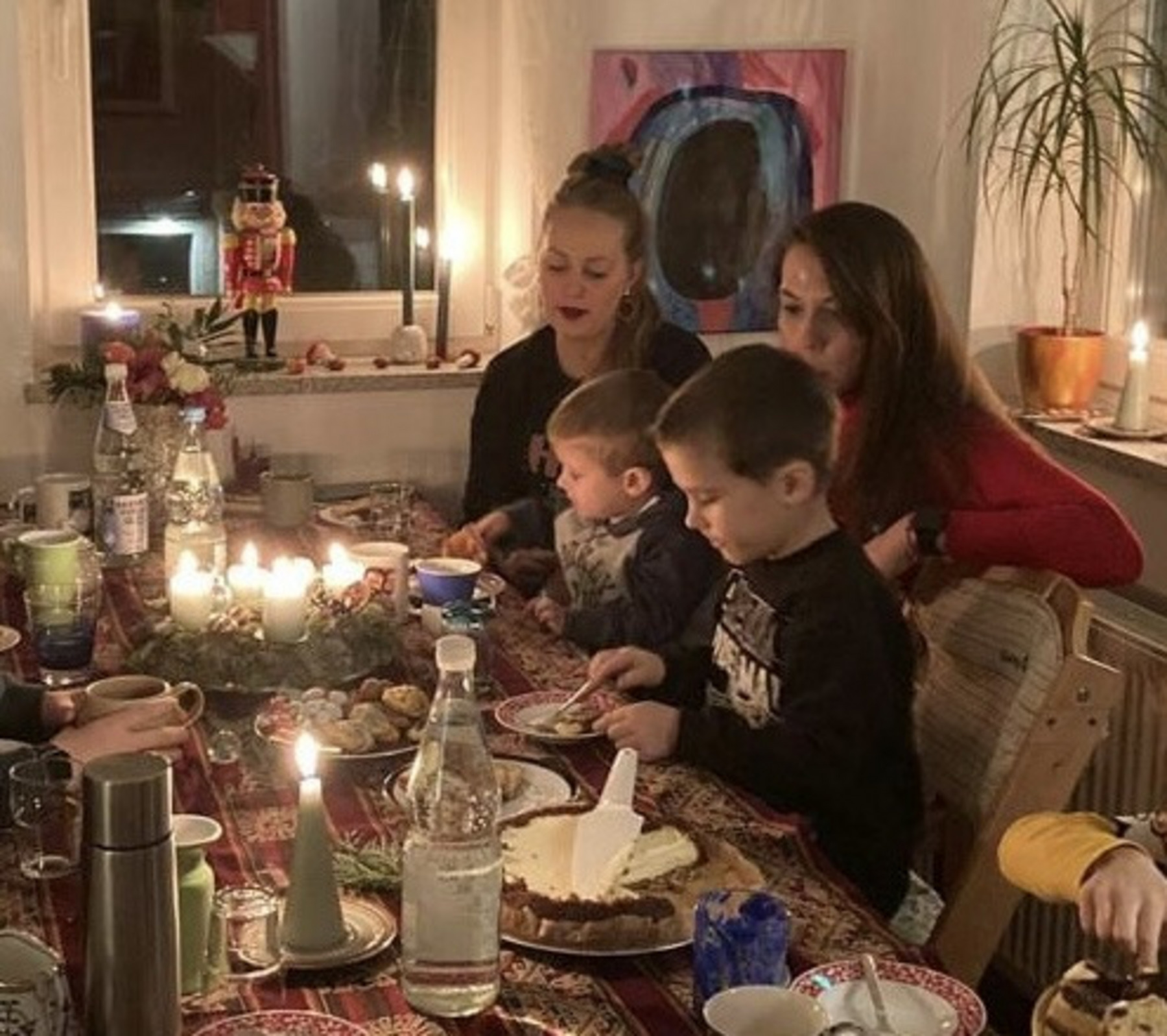 Maren, Hanna und ihre beiden Söhne sitzen an einem Tisch. Dieser ist geschmückt mit einem Adventskranz, Plätzchen und Kuchen sowie anderen Speisen und Getränken.