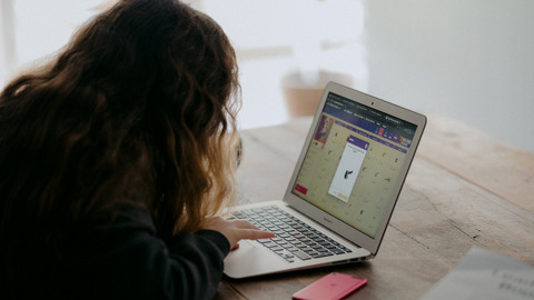 Eine junge Frau schaut auf ihren Laptop, in dessen Browserfenster eine Online-Lernanwendungen geöffnet ist