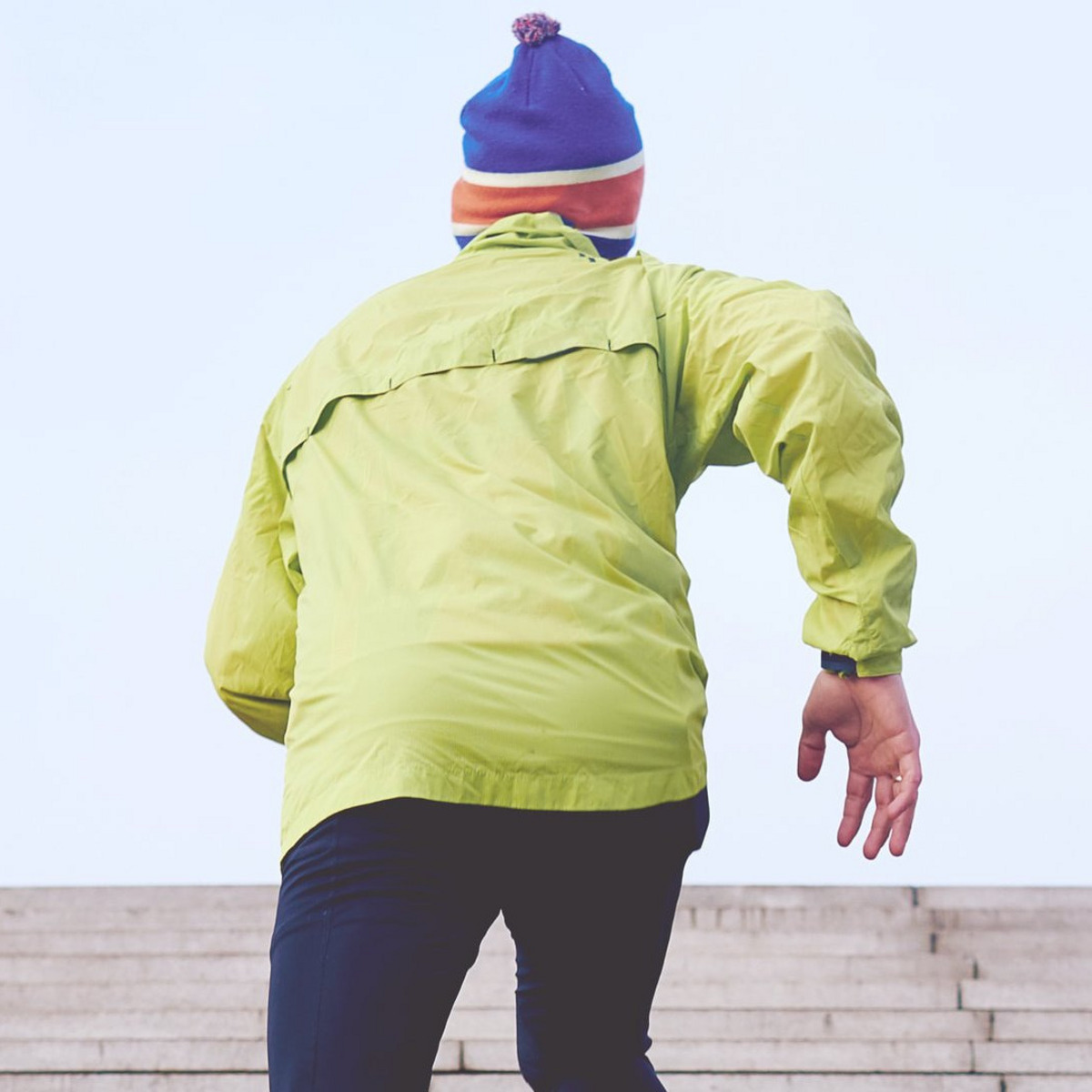 Ein Mann in einer gelben Funktionsjacke joggt eine Treppe hoch.