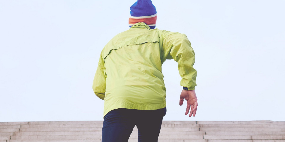Ein Mann in einer gelben Funktionsjacke joggt eine Treppe hoch.