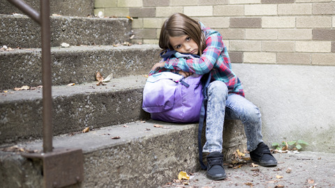 Ein Mädchen mit braunen Haaren sitzt auf einer Treppe und sieht traurig aus.