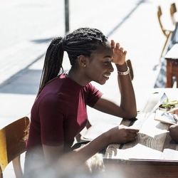 Ein junges Paar sitzt an einem Tisch vor einem Café und unterhält sich. Die Frau trägt einen weinroten Pullover und lächelt, während der Mann ihr zugewandt in einem hellen Hemd am Tisch sitzt.