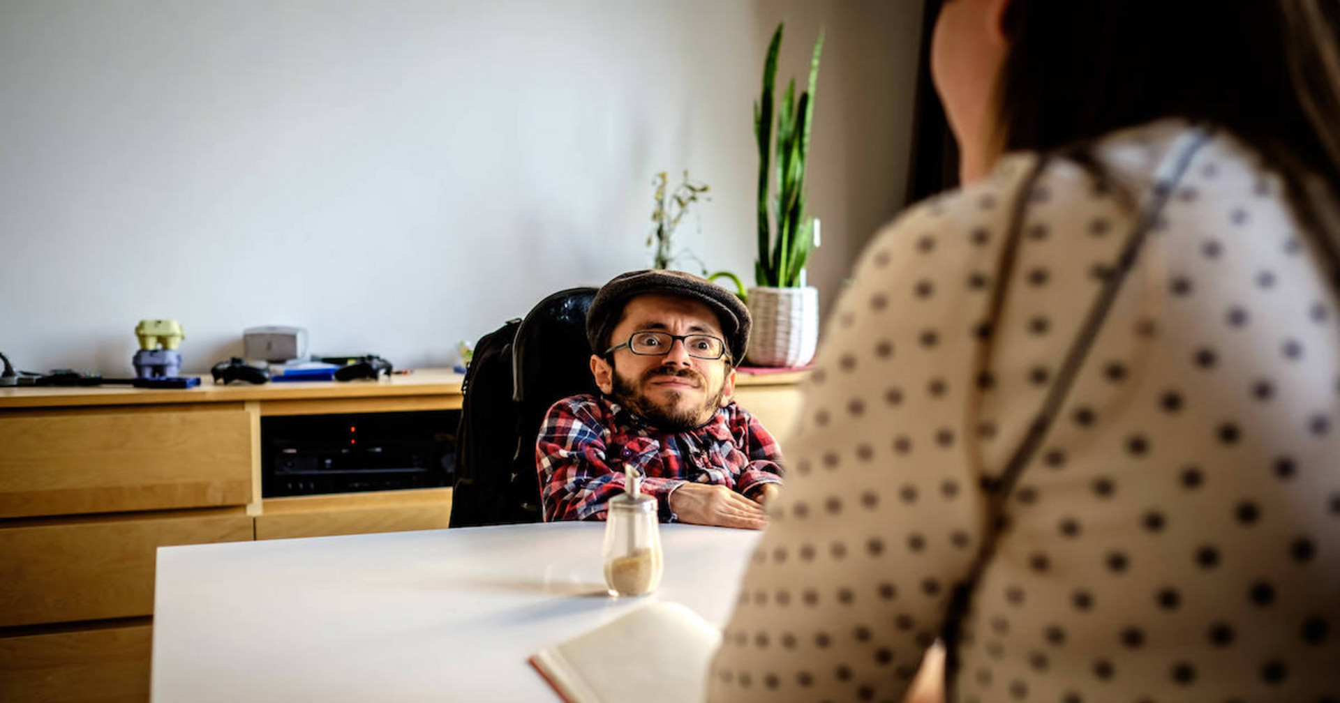 Ein Mann mit Brille und Kappe sitzt gegenüber von einer anderen Person an einem Tisch.