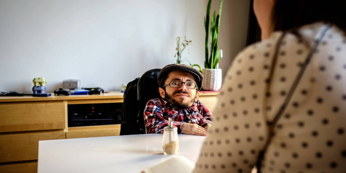 Ein Mann mit Brille und Kappe sitzt gegenüber von einer anderen Person an einem Tisch.