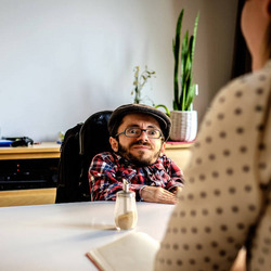 Ein Mann mit Brille und Kappe sitzt gegenüber von einer anderen Person an einem Tisch.