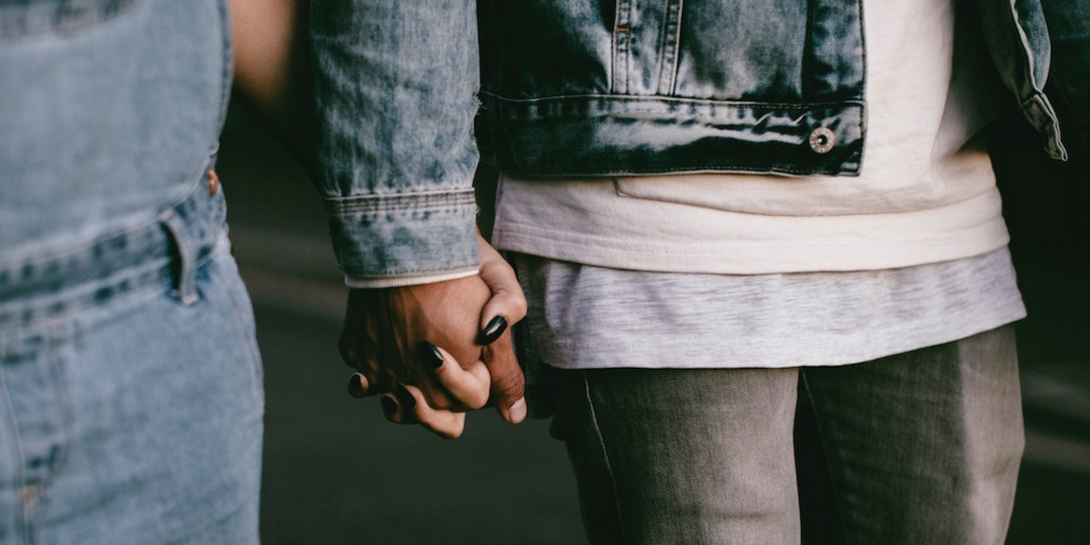 Zwei Personen mit Denim-Klamotten halten Händchen.