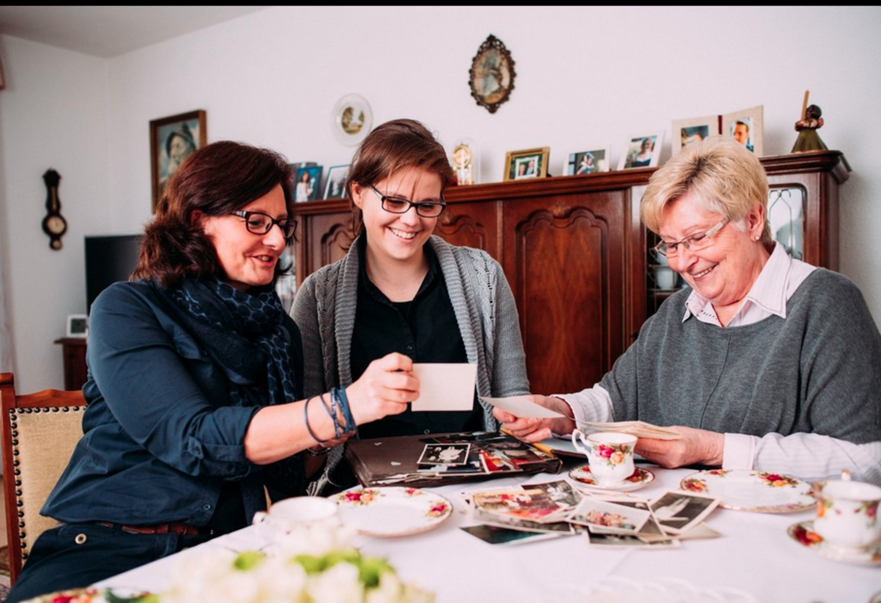 Drei Menschen sitzen an einem Tisch und schauen sich Fotos an