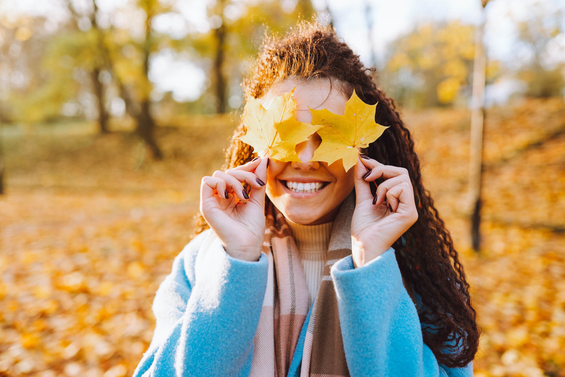 Junge Frau in einem herbstlichen Park hält sich bunte Blätter vor die Augen